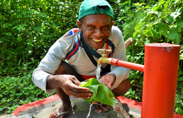 A smiling man wearing a green baseball cap crouching in front of a red and yellow tap